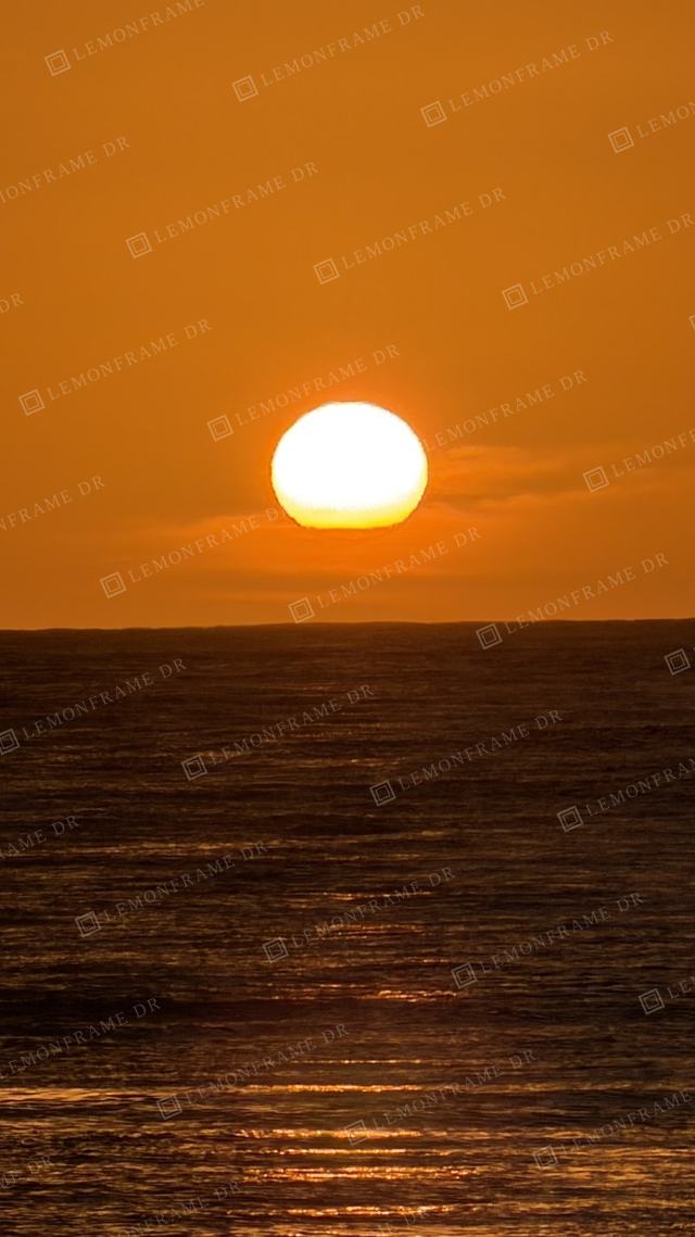 Sol blanco sobre un cielo naranja intenso y el mar