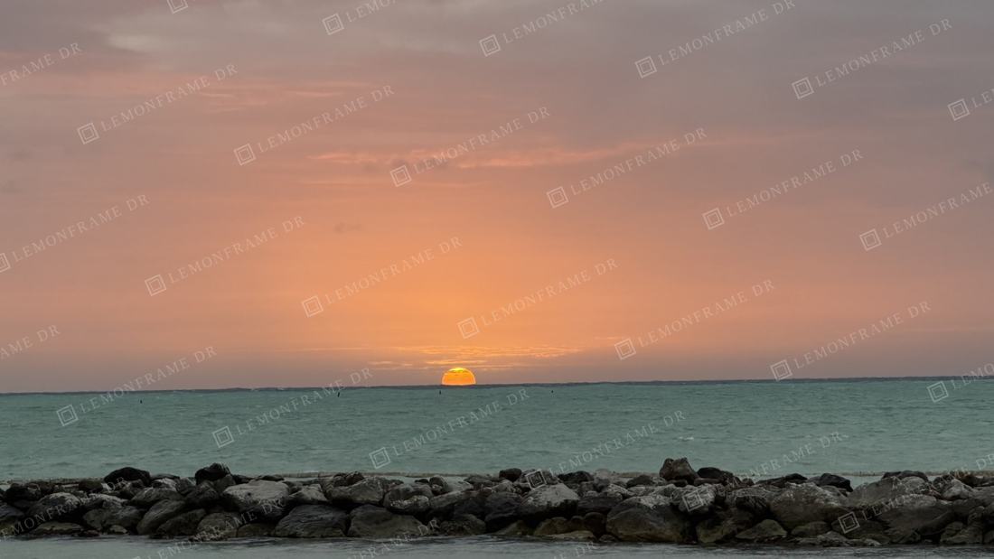 Sol rosado sobre el mar turquesa y el rompeolas